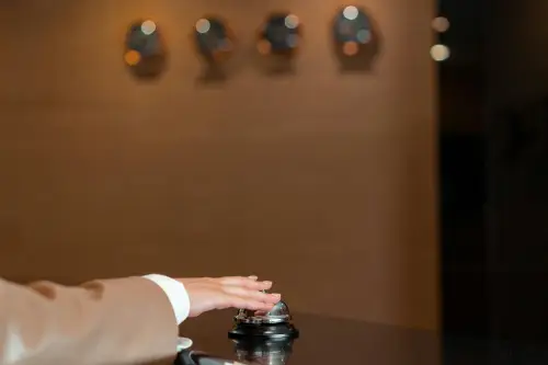 A hotel guest's hand reaching for a service bell at a reception desk.